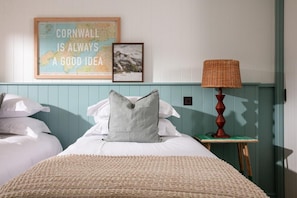 A bedroom with a bed, pillows, a framed map, a lamp, and a small table. - 4 Bed in Watergate Bay (oc-b584453) (Tregurrian)