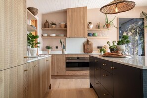 A modern kitchen with wooden cabinets, a central island, and various decorative items. - 4 Bed in Watergate Bay (oc-b584453) (Tregurrian)