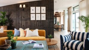 En moderne stue med en trævæg, en sofa, en stribet lænestol og et sofabord med bøger og planter.