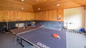 Uma mesa de pingue-pongue com equipamentos de ginástica e pesos em um cômodo com paredes e teto de madeira.