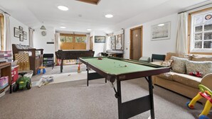 Um quarto com mesa de bilhar, sofá e janela com cortinas.