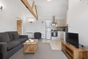 A modern living room with a grey sofa, a wooden coffee table, and a TV on a wooden stand. - 1 Bed in Milton Abbas (oc-c35017) (Milton Abbas)
