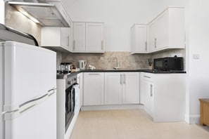 A modern kitchen with white cabinets, a black countertop, a microwave, and a stove. - 1 Bed in Milton Abbas (oc-c35017) (Milton Abbas)