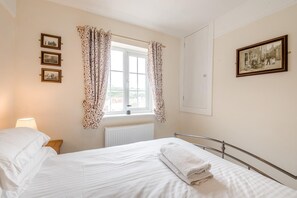 A hotel room with a bed, a window with curtains, a radiator, and framed pictures on the wall. - 3 Bed in Whitby (oc-c40269) (Whitby)