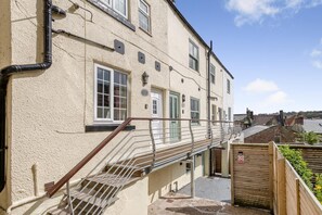 A building with a staircase leading to a landing, a wooden fence, and a clear sky. - 3 Bed in Whitby (oc-c40269) (Whitby)