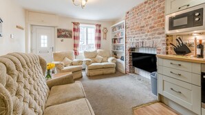 A living room with a sofa, armchairs, a fireplace, a television, and a kitchen area with a microwave. - 3 Bed in Whitby (oc-c40269) (Whitby)