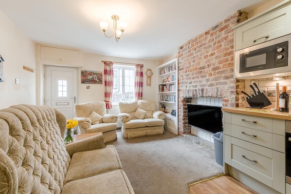 A living room with a sofa, armchairs, a fireplace, a television, and a kitchen area with a microwave. - 3 Bed in Whitby (oc-c40269) (Whitby)