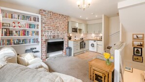 A modern living room with a fireplace, a bookshelf, a dining area, and a kitchen. - 3 Bed in Whitby (oc-c40269) (Whitby)