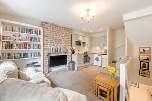 A modern living room with a fireplace, a bookshelf, a dining area, and a kitchen. - 3 Bed in Whitby (oc-c40269) (Whitby)