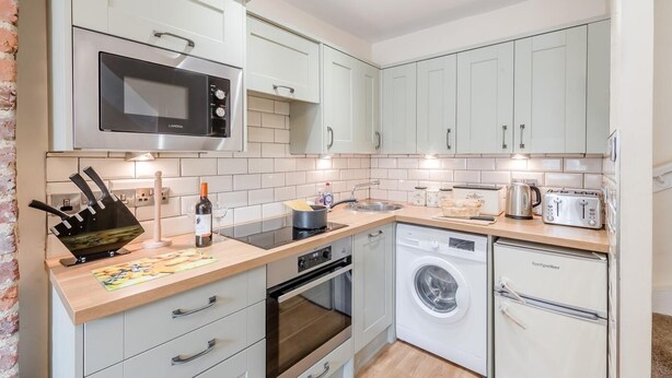 A compact kitchen with white cabinets, a microwave, a toaster, a kettle, and a washing machine. - 3 Bed in Whitby (oc-c40269) (Whitby)