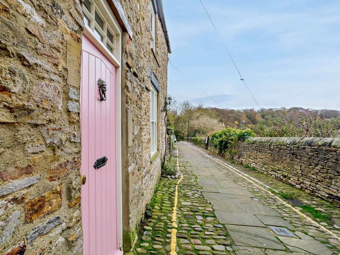 A narrow cobblestone street with a pink door on a stone building.