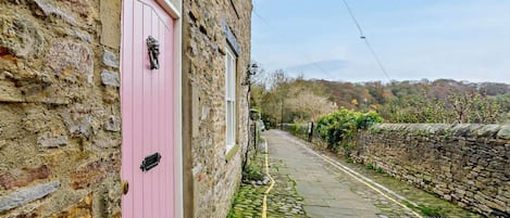 A narrow cobblestone street with a pink door on a stone building.