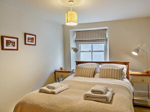 A neatly made bed with a textured blanket, a bedside lamp, and a window with a patterned curtain. - 3 Bed in Richmond (oc-g0028) (Richmond)