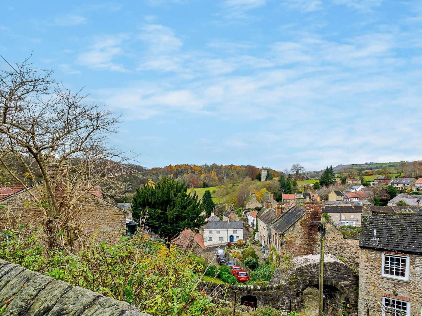 A rural village with stone buildings, a stone wall, and a hill in the background.