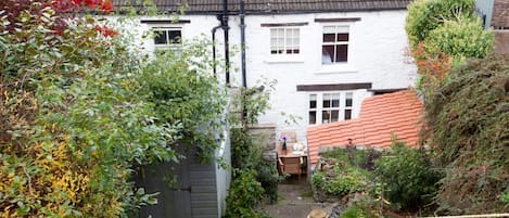 A white house with a tiled roof, a wooden fence, and a garden area with various plants and a small table.