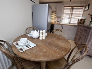 A dining area with a round wooden table, white tableware, and a kitchen in the background. - 2 Bed in Whitby (oc-g0130) (Whitby)