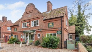 A traditional brick building with a green entrance, a clock, and a sign indicating it's a guest clock cafe and shop. - 3 Bed in Guist (oc-h33647) (Guist)