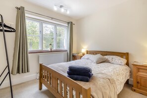 Ein Schlafzimmer mit einem hölzernen Bett, einem Nachttisch, einem Fenster mit Vorhängen und einer Heizung.