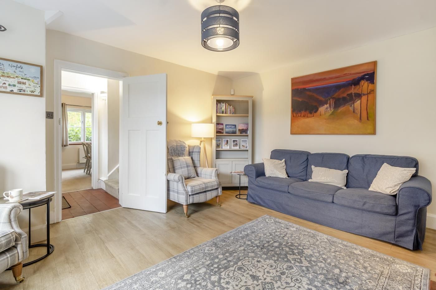 A living room with a sofa, armchair, and a rug. There is a bookshelf and a painting on the wall.