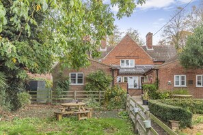 A brick house with a tiled roof, a wooden fence, and a garden with a picnic table. - 3 Bed in Guist (oc-h33647) (Guist)