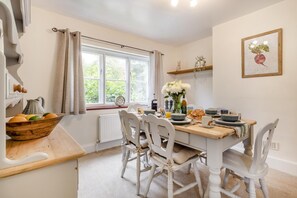A dining area with a wooden table, white chairs, and a window with curtains. - 3 Bed in Guist (oc-h33647) (Guist)