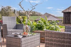 An outdoor seating area with wicker chairs and a glass table, featuring a bottle and glasses, and a bowl of fruit. - 1 Bed in Milton Abbas (oc-l35018) (Milton Abbas)