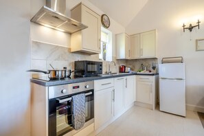 A modern kitchen with white cabinetry, a stainless steel range hood, a microwave, an oven, a refrigerator, and a clock on the wall. - 1 Bed in Milton Abbas (oc-l35018) (Milton Abbas)