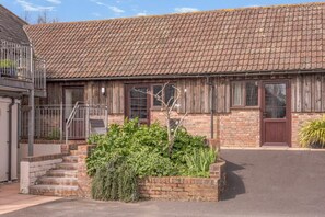 A two-story building with a brick facade, a tiled roof, and a small garden area with steps leading to the entrance. - 1 Bed in Milton Abbas (oc-l35018) (Milton Abbas)