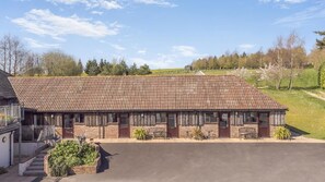 A two-story building with a tiled roof, a front porch with benches, and a small garden area. - 1 Bed in Milton Abbas (oc-l35018) (Milton Abbas)