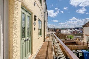 Ein Balkon mit Blick auf eine Stadt, eine Tür mit Klingelschild und ein Geländer.