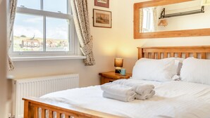 A neatly made bed with white linens, a bedside lamp, and a window with curtains. - 2 Bed in Whitby (oc-m32879) (Whitby)