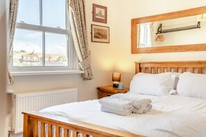 Ein ordentlich bezogenes Bett mit weißen Laken, einer Nachttischlampe und einem Fenster mit Vorhängen.