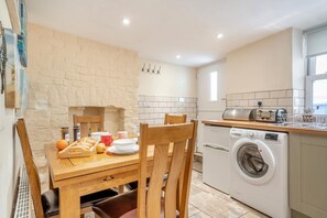 A compact kitchen with a washing machine, a dining table with chairs, and a stone wall. - 2 Bed in Whitby (oc-m32879) (Whitby)