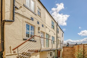 Ein zweistöckiges Gebäude mit einer Treppe, die zu einem Balkon führt, mehreren Fenstern und einem hölzernen Zaun.