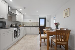 A modern kitchen with white cabinets, a dining table with chairs, and a view through the door. - 1 Bed in Milton Abbas (oc-o35015) (Milton Abbas)