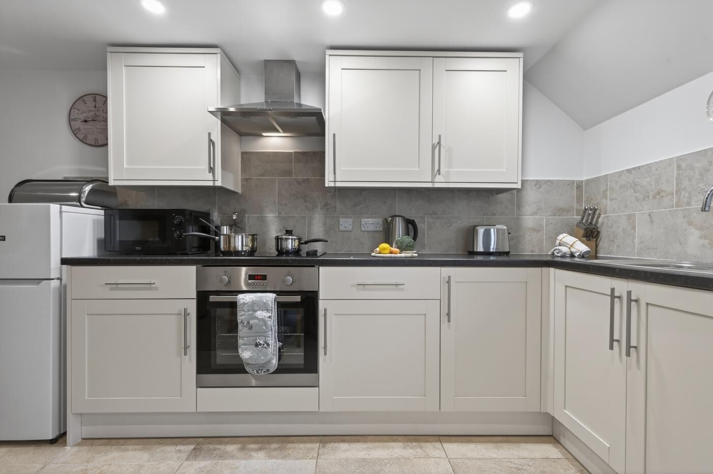 Una cocina moderna con gabinetes blancos, una campana extractora de acero inoxidable y un horno empotrado.