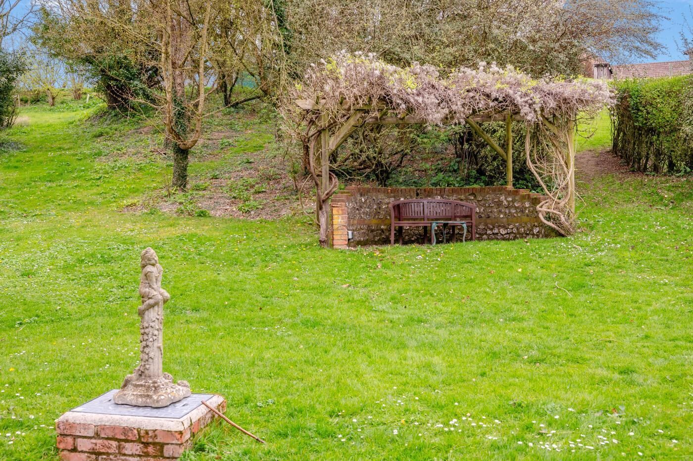 Ein Garten mit einer Statue, einer Holzpergola und einer Bank.