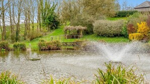 Ein Teich mit einer Springbrunnenanlage, umgeben von Grünpflanzen und einer Holzhütte.