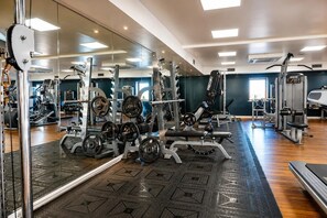 Ein Fitnessraum mit unterschiedlichen Trainingsgeräten, einer Spiegelwand und einem gemusterten Boden.