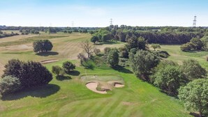An aerial view of a golf course with sand bunkers, trees, and power lines in the background. - 1 Bed in Barnham Broom (oc-p42617) (Barnham Broom)