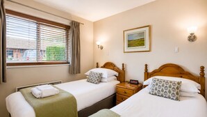 A hotel room with two beds, a window with blinds, a bedside table with a clock, and a framed picture on the wall. - 1 Bed in Barnham Broom (oc-p42617) (Barnham Broom)