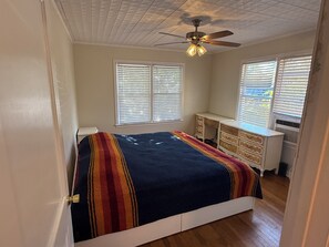 Quarto com cama, escrivaninha e ventoinha no teto.