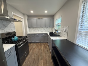 A modern kitchen with grey cabinets, a black stove, and a marble backsplash.