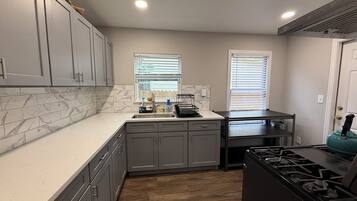 A kitchen with grey cabinets, a marble backsplash, a sink, a stove, and a window with blinds.