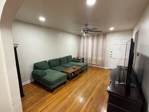 Una sala de estar con un sofá modular, una mesa de centro de madera, un ventilador de techo y un televisor sobre un mueble bajo.