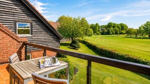 Una terraza de madera con una mesa y sillas, con vistas a un césped cuidado y un campo de golf.