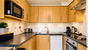 Una cocina moderna con armarios de madera, encimera negra, microondas integrado, tostadora, lavaplatos y lavabo.