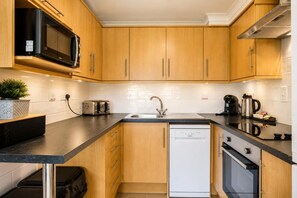 A modern kitchen with wooden cabinets, a black countertop, a built-in microwave, a toaster, a sink, and a dishwasher. - 2 Bed in Barnham Broom (oc-s42613) (Barnham Broom)