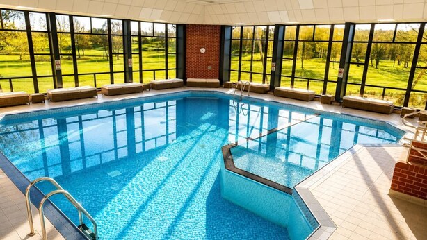 Una piscina interior con vistas despejadas a un campo de golf a través de amplios ventanales.