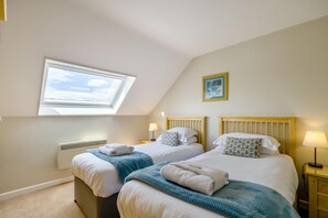 A bedroom with two beds, a skylight, a radiator, and a small painting on the wall. - 3 Bed in Barnham Broom (oc-s42615) (Barnham Broom)
